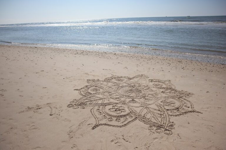 Ein Mandala in den Sand gezeichnet am Meer. Die Wellen rollen ans Ufer.